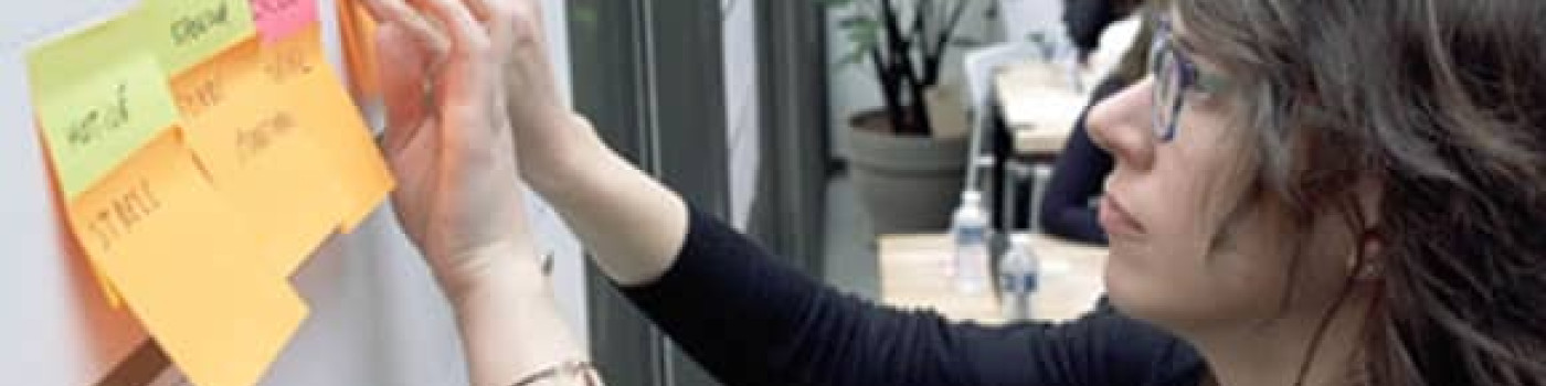 Jeune femme face à un tableau de post-it pour imaginer l’Ecole de demain, NEOMA Business School